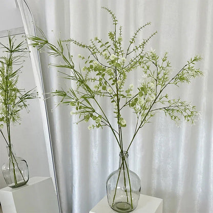 Clear glass vase with green branches against a white curtain background