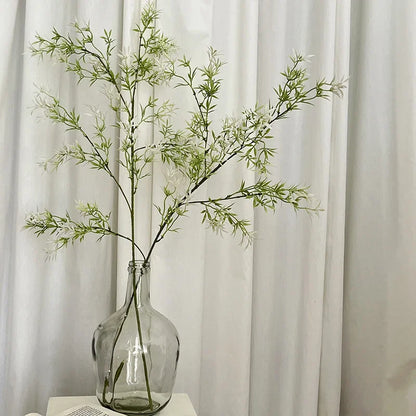 Clear glass vase with green branches against a white curtain background