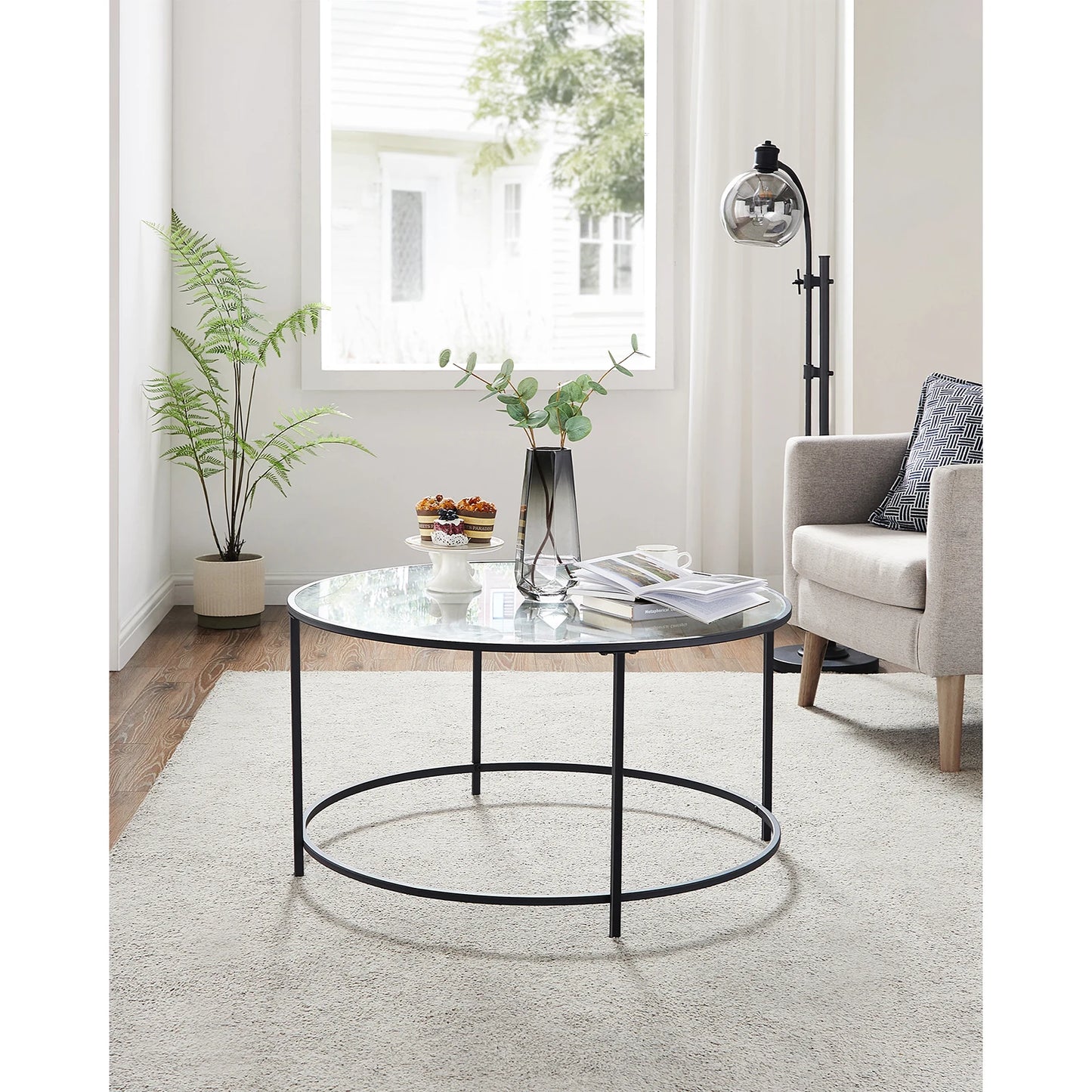 Round glass coffee table with black metal frame in a living room setting.