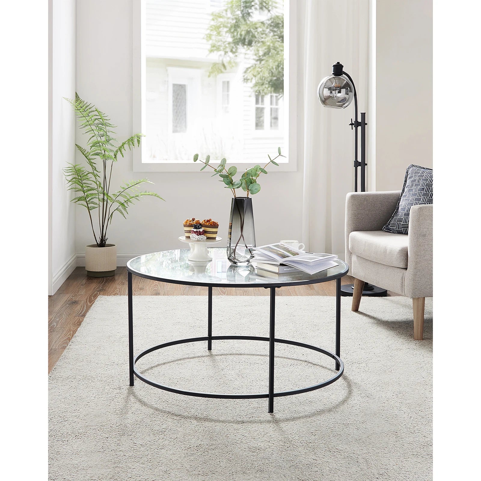 Round glass coffee table with black metal frame in a living room setting.